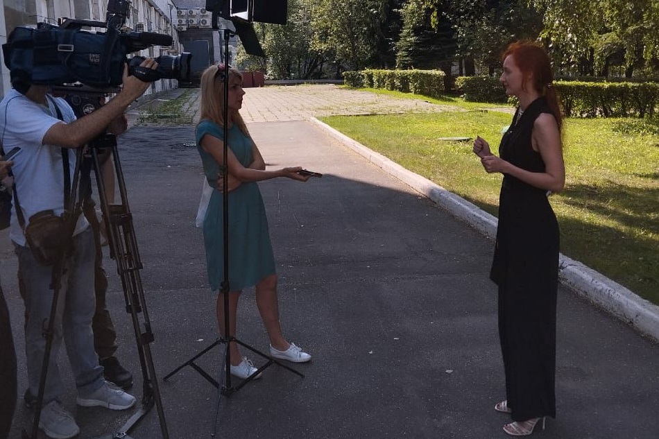 Ирина Головачёва даёт интервью тележурналистам: на улице перед зданием на фоне сквера
